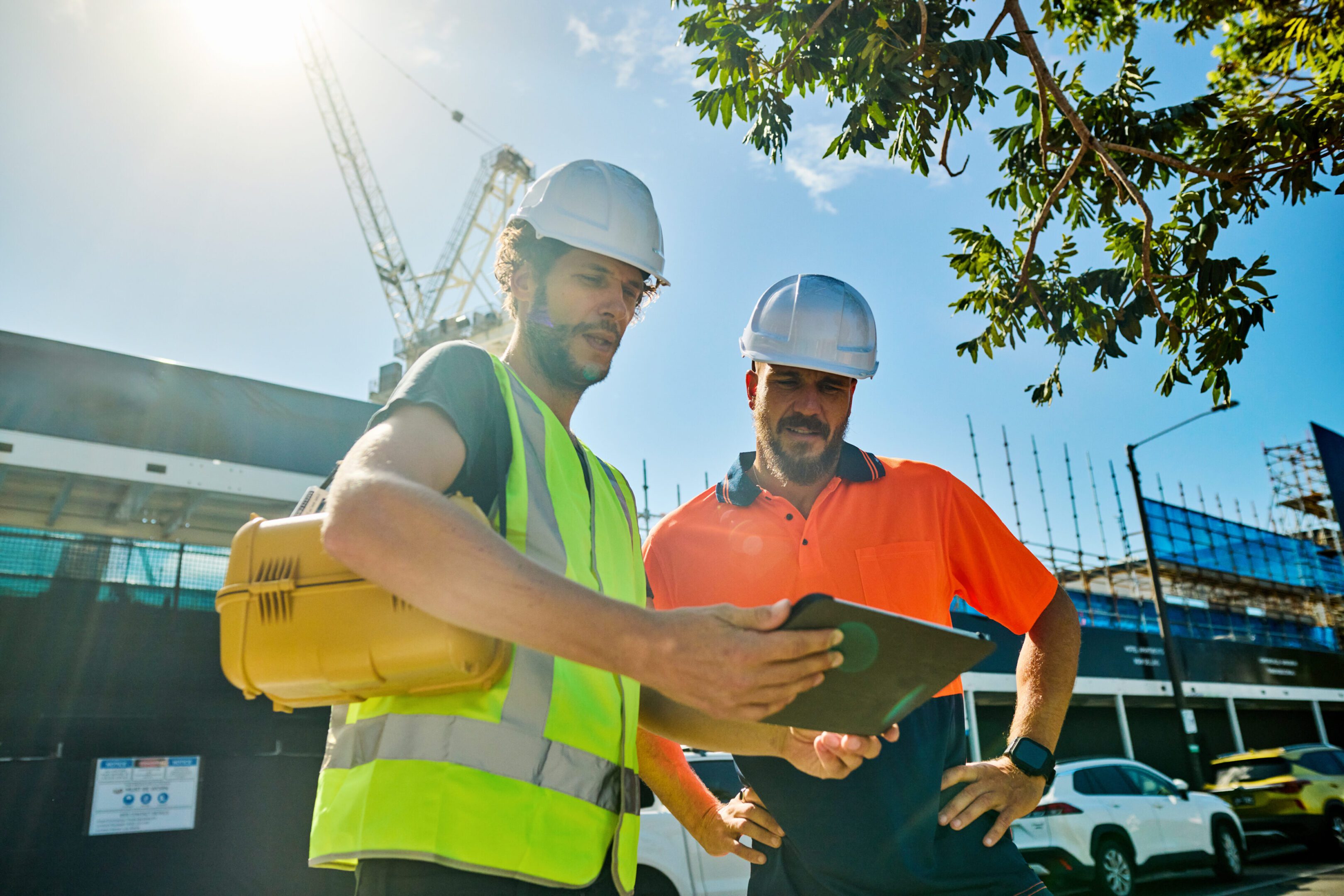 Two construction workers reviewing plans on a tablet at a building site.