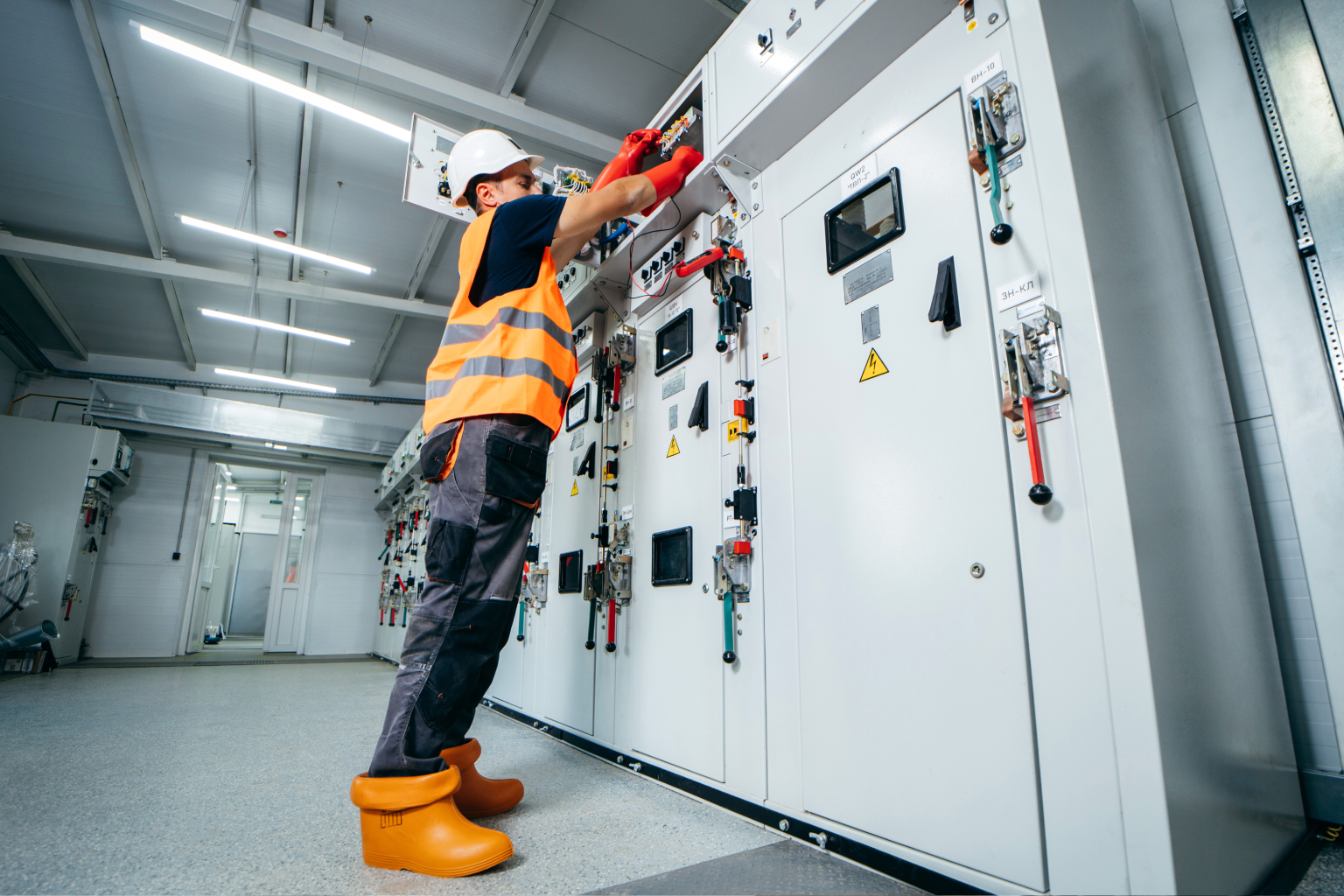 Electrician in safety gear working on electrical control panels.